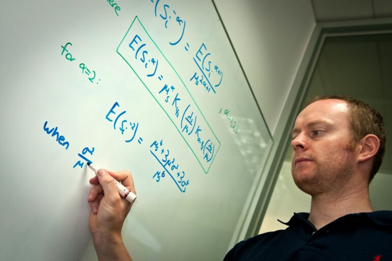 Male researcher writing formulae on whiteboard.